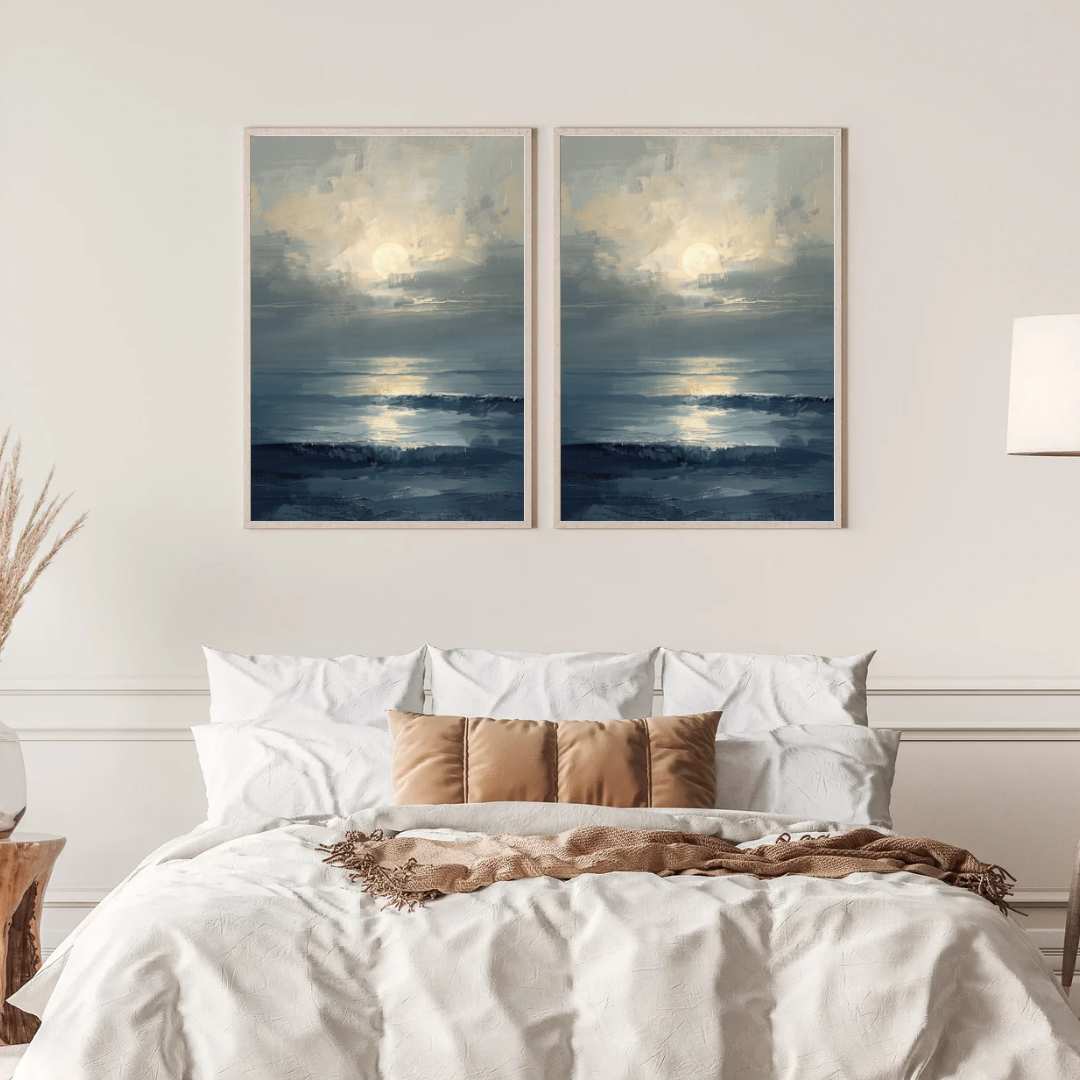 Maanlicht zee schilderij met grijsblauw water en gouden maangloed in twee gouden lijsten naast elkaar aan witte muur boven bed met linnen beddengoed – sereen wall art slaapkamer