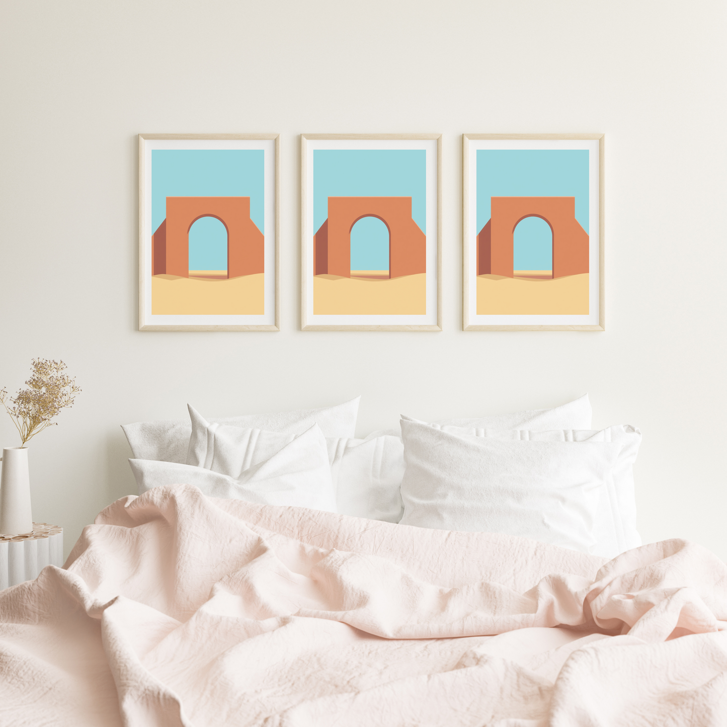 Marokkaanse poort schilderij met terracotta boog en turquoise lucht in drie witte lijsten naast elkaar hangend aan witte muur boven bed met roze beddengoed – mediterraan wall art logeerkamer