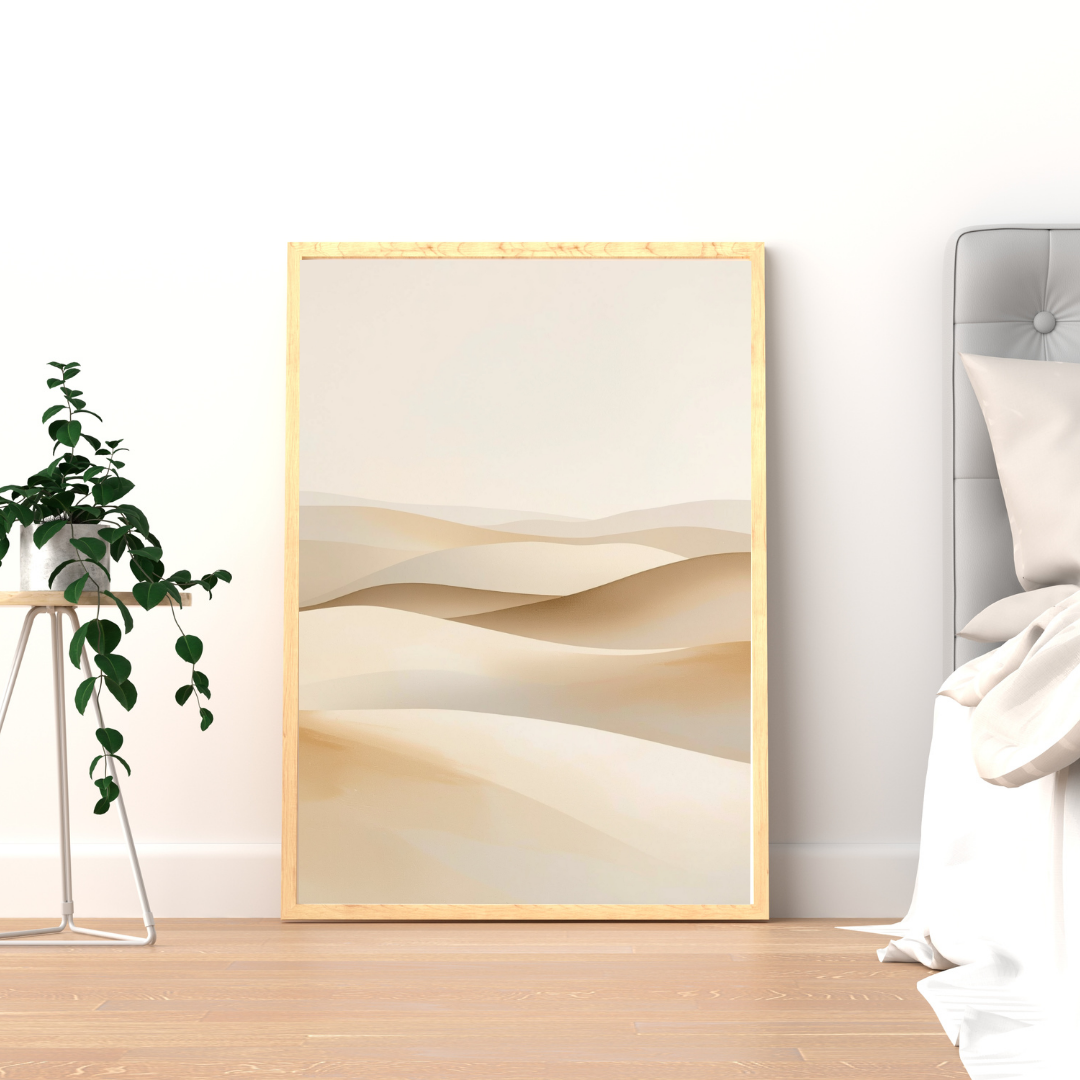 Abstract zandduinen schilderij met zachte crème en beige duinlagen in gouden lijst staand op houten vloer naast groene plant – sereen wall art logeerkamer