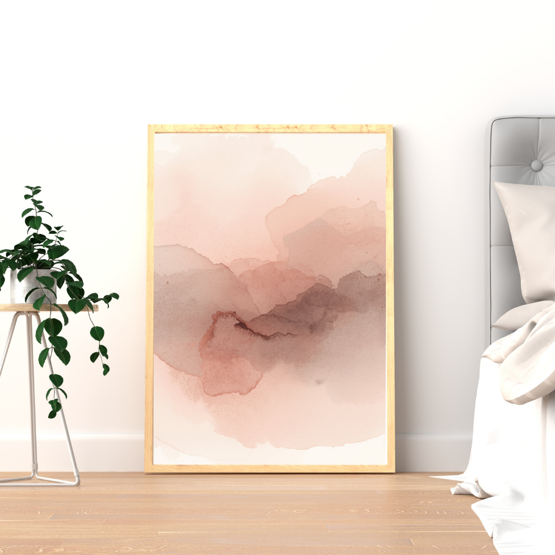 Abstract roze mauve schilderij met vloeiende aquarelvlekken in roze en mauve in gouden lijst staand op houten vloer naast groene plant – sereen wall art logeerkamer