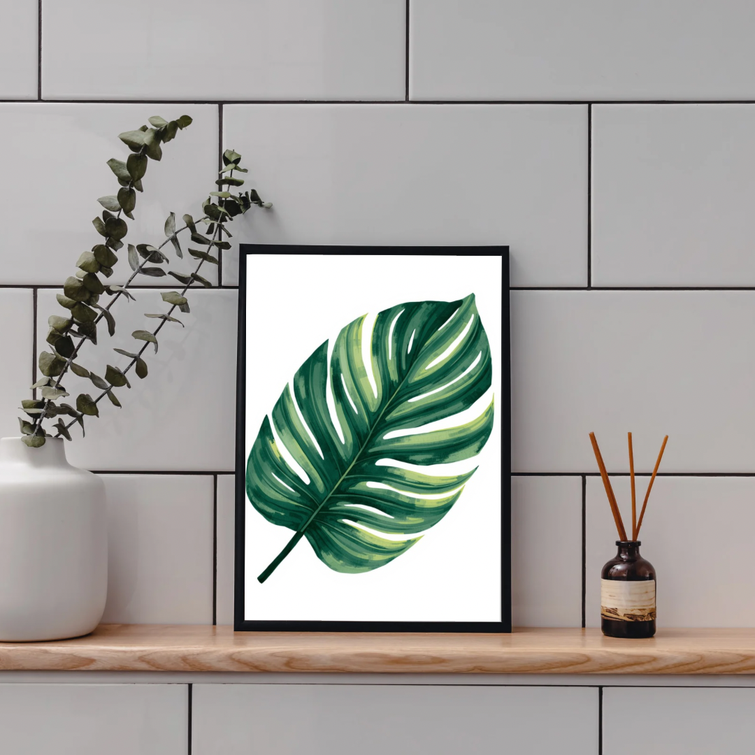 Monstera blad schilderij in zwarte lijst op houten plank aan grijze tegelmuur naast droogbloemen en waxinelichtje – botanisch aquarel wall art toilet