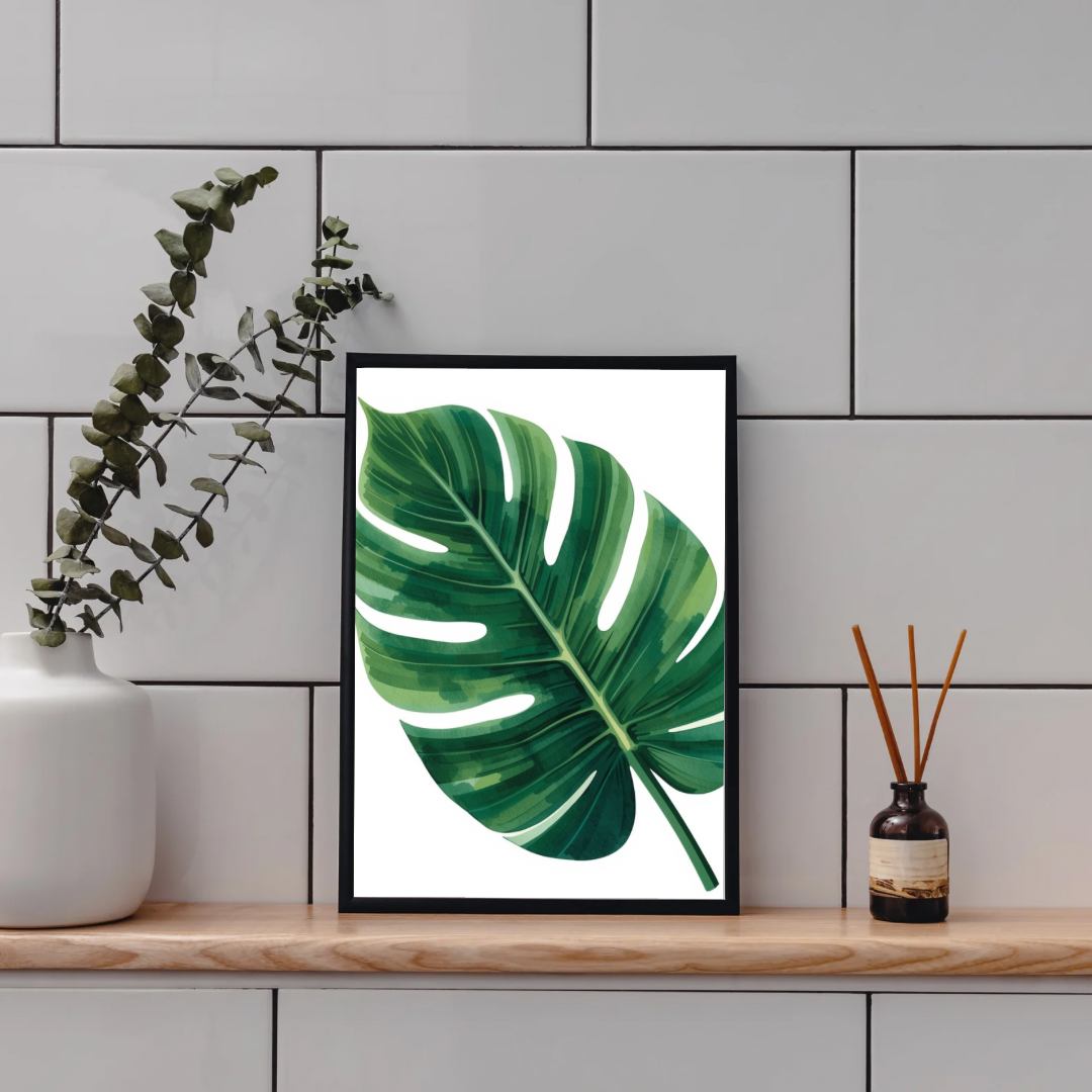 Monstera blad schilderij in zwarte lijst staand op houten plank aan grijze tegelmuur naast witte vaas met eucalyptus en bruine diffuser – botanisch aquarel wall art toilet