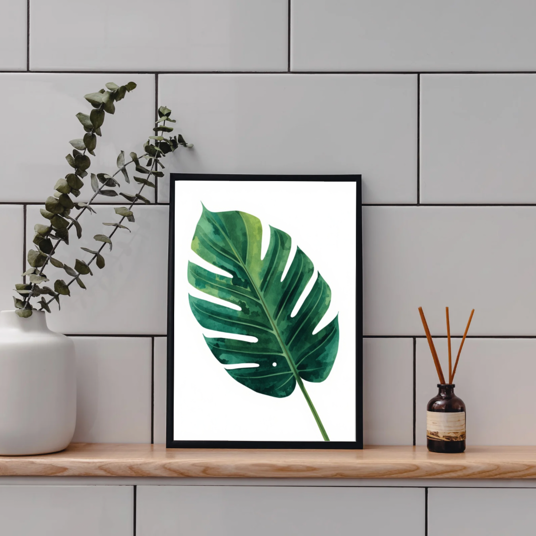 Monstera blad schilderij in zwarte lijst staand op houten plank aan grijze tegelmuur naast witte vaas met eucalyptus en bruine diffuser – botanisch aquarel wall art toilet