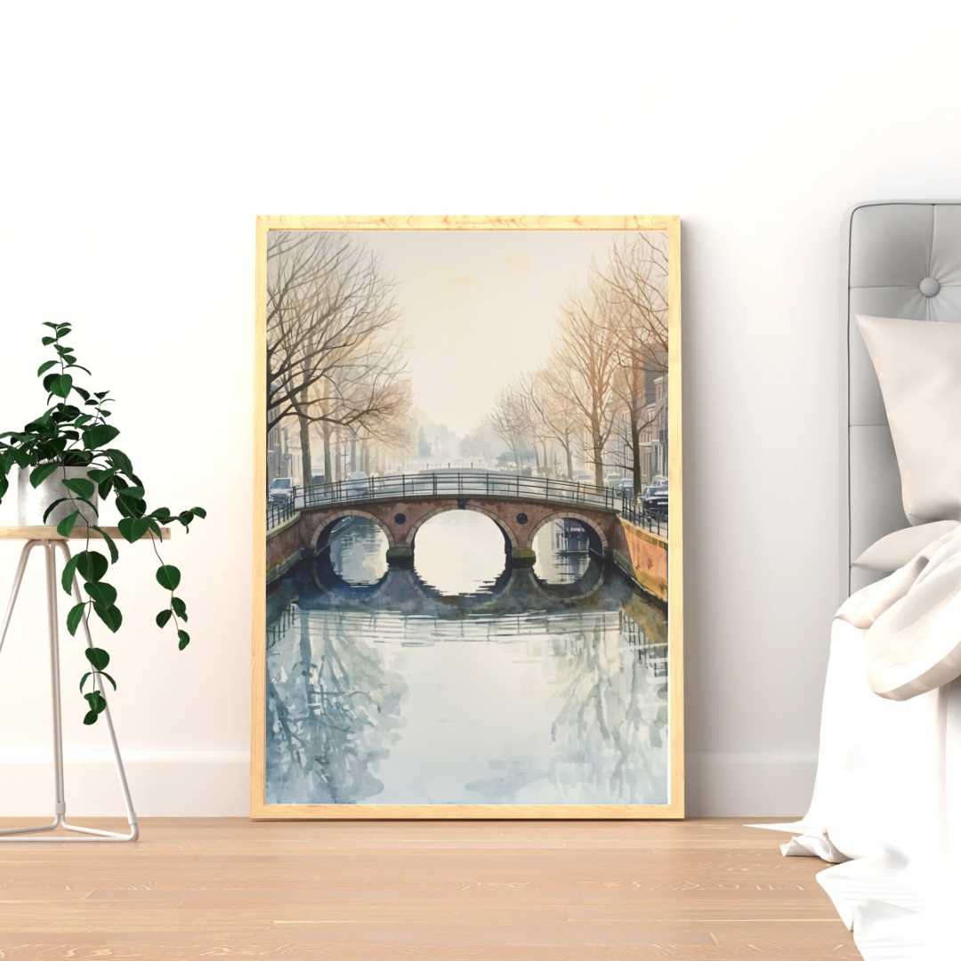Gracht brug schilderij in donkere lijst staand op lichte houten vloer tegen witte muur naast hangplant en bed – aquarel wall art slaapkamer
