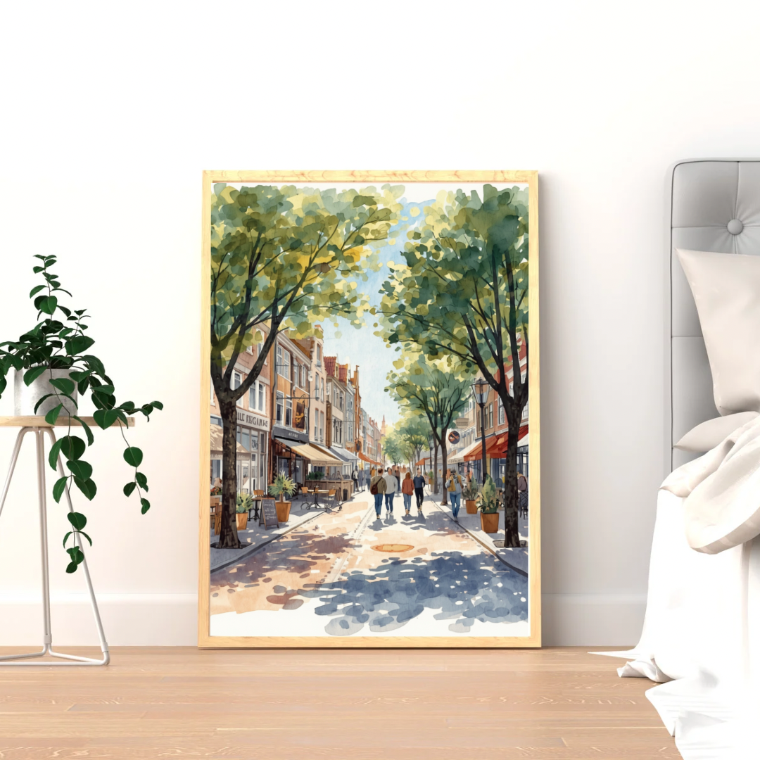 Apeldoorn winkelstraat schilderij in witte lijst staand op lichte houten vloer tegen witte muur naast hangplant en bed – aquarel wall art slaapkamer
