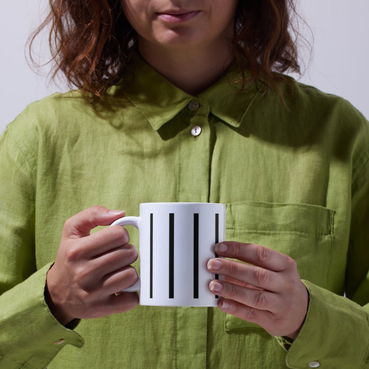 Persoon in een groen overhemd met een witte koffiemok met zwarte strepen