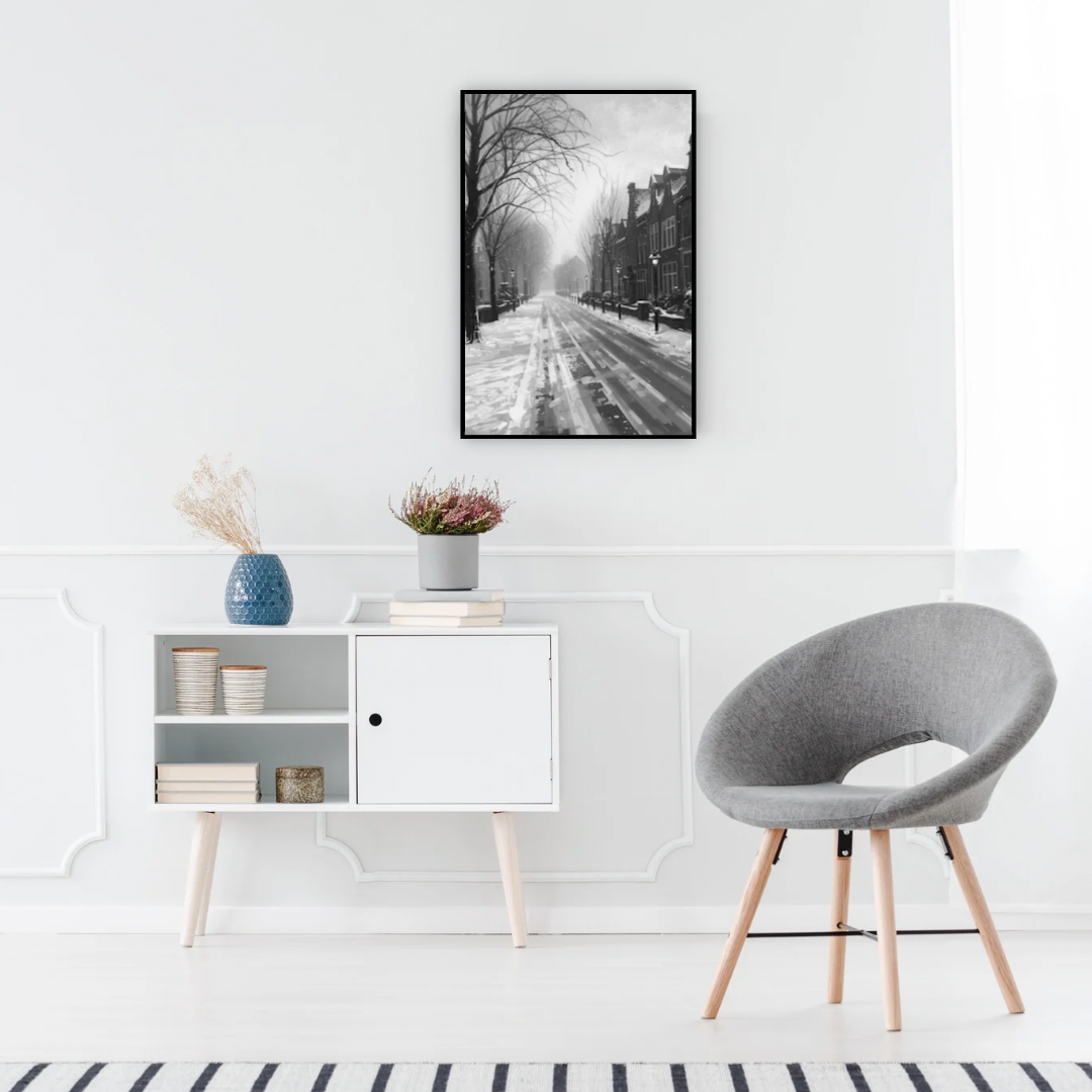 Alkmaar sneeuwstraat schilderij in zwarte lijst aan witte muur boven wit dressoir met grijze stoel en blauwe vaas in minimalistische ruimte – zwart-wit wall art print
