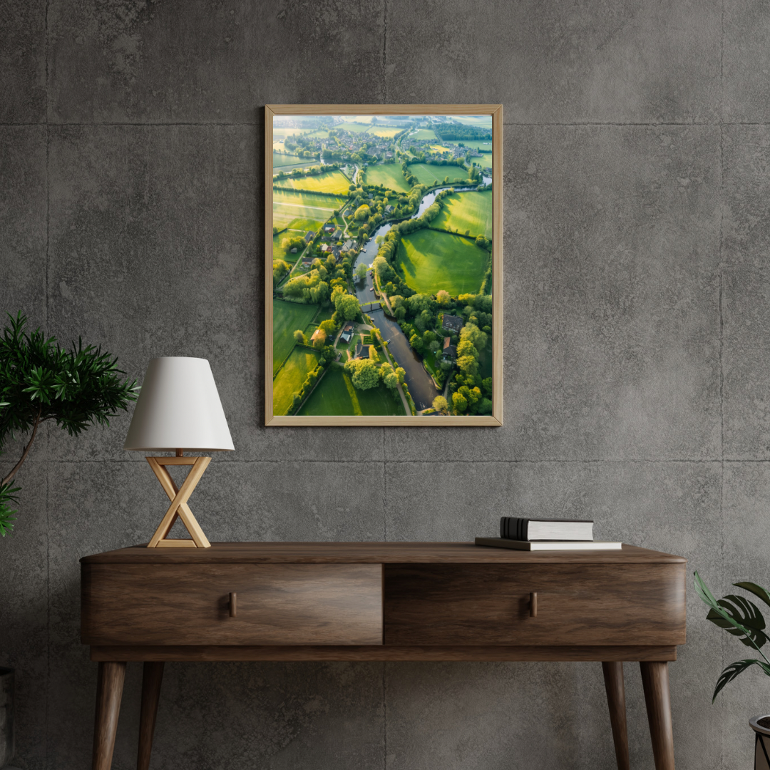 Weelderig groen landschap luchtfoto schilderij in zwarte lijst aan donkere antraciet muur boven donker houten bureau met witte lamp en groene plant – wall art print studeerkamer
