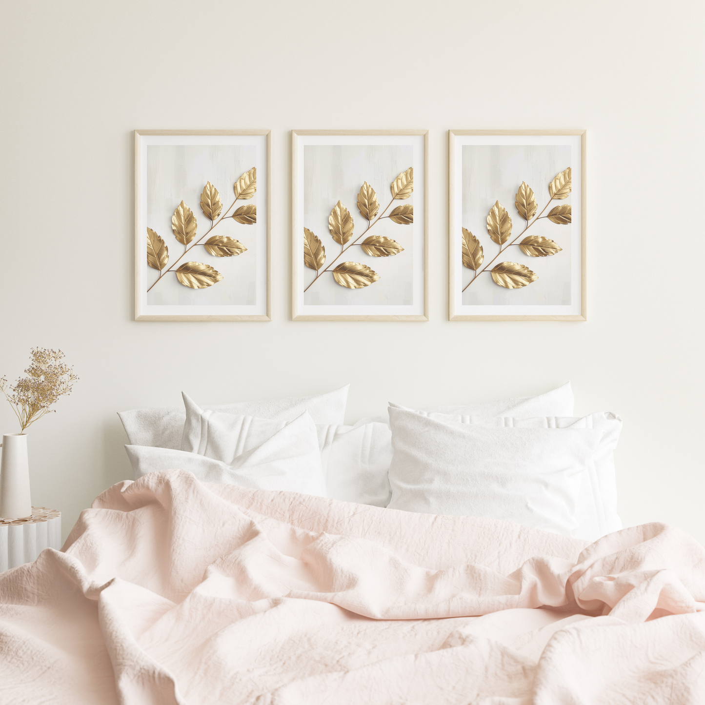 Gouden bladeren schilderij met glanzende gouden bladtak in drie witte lijsten naast elkaar hangend aan witte muur boven bed met roze beddengoed – botanisch wall art logeerkamer
