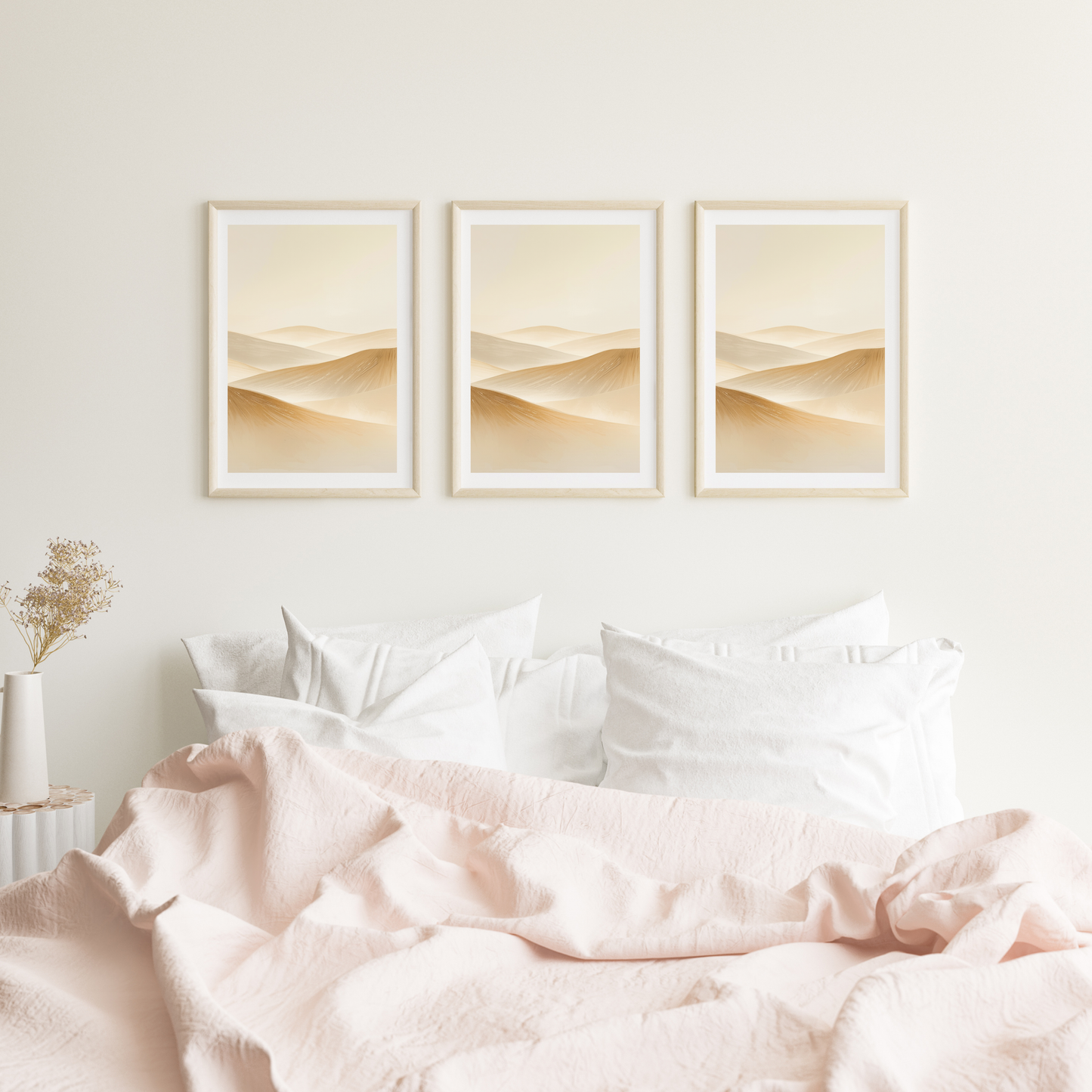 Abstract woestijn schilderij met zachte beige zandgolven in drie witte lijsten naast elkaar hangend aan witte muur boven bed met roze beddengoed – sereen wall art logeerkamer
