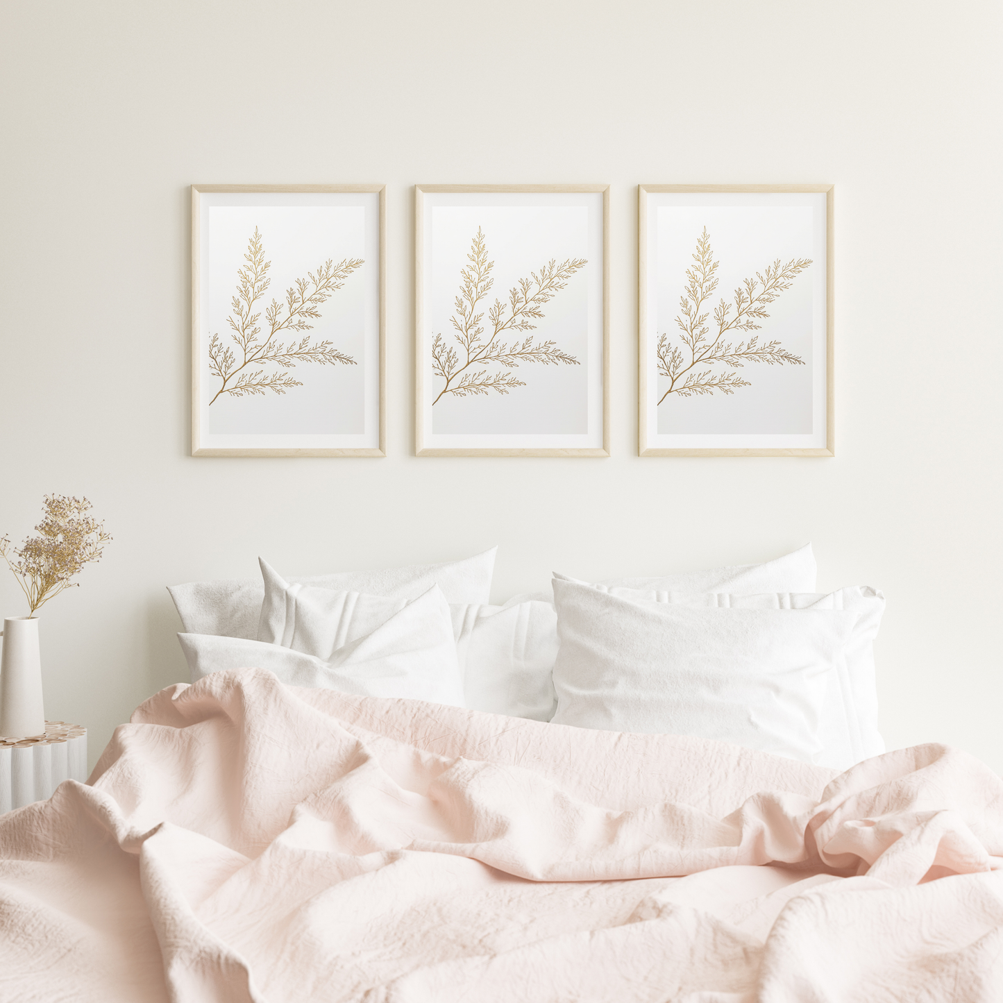 Botanische olijftak schilderij met fijne gouden olijftak en delicate blaadjes in drie witte lijsten naast elkaar hangend aan witte muur boven bed met roze beddengoed – botanisch wall art logeerkamer
