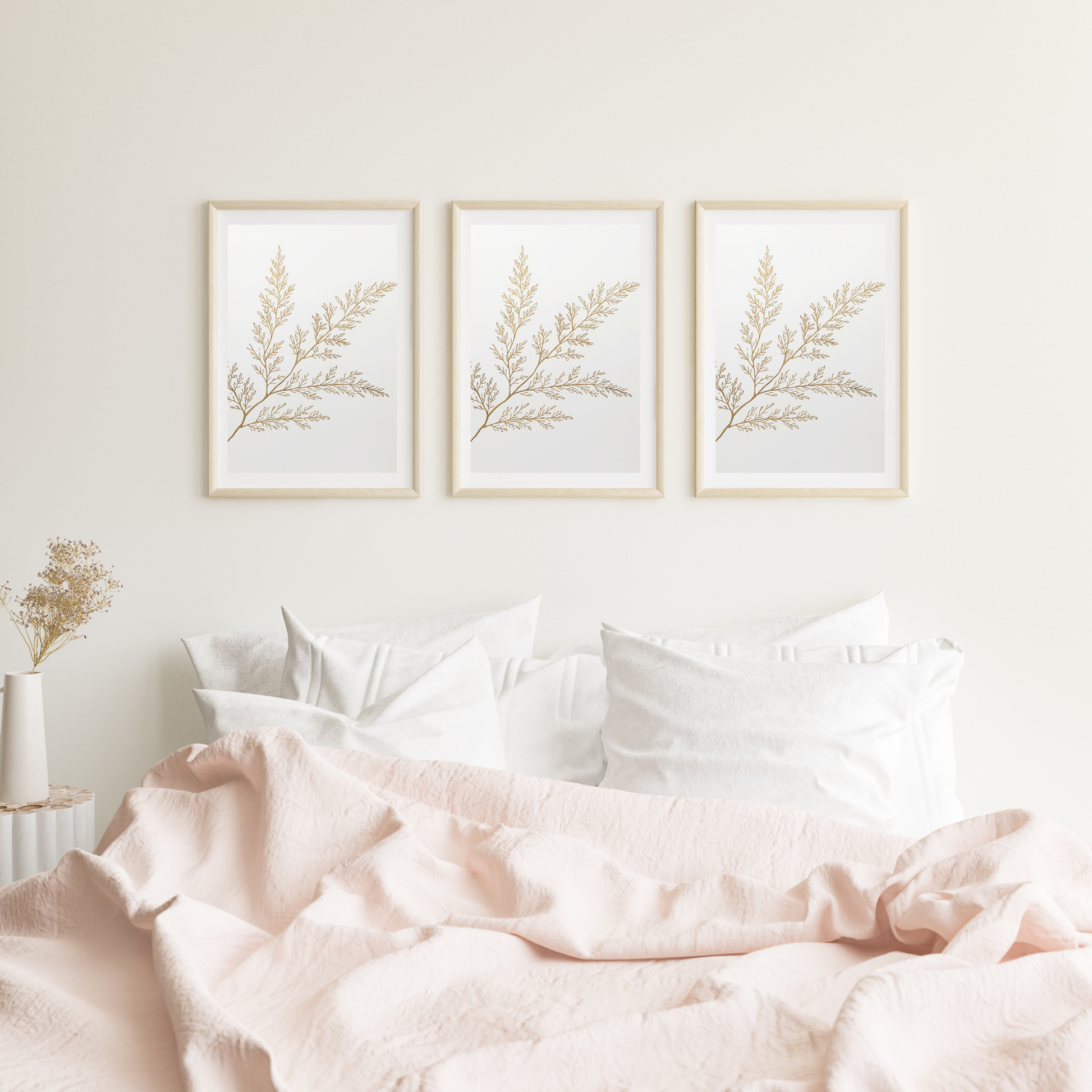 Botanische olijftak schilderij met fijne gouden olijftak en delicate blaadjes in drie witte lijsten naast elkaar hangend aan witte muur boven bed met roze beddengoed – botanisch wall art logeerkamer
