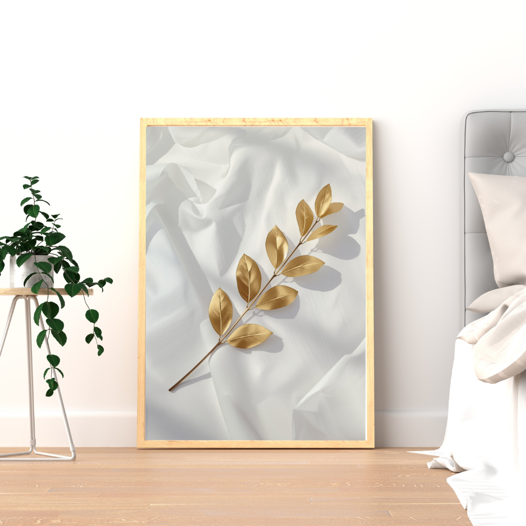 Gouden bladtak op wit satijn schilderij met warme goudbeige tak en zijdezacht fond in gouden lijst staand op houten vloer naast groene plant – luxueus wall art logeerkamer
