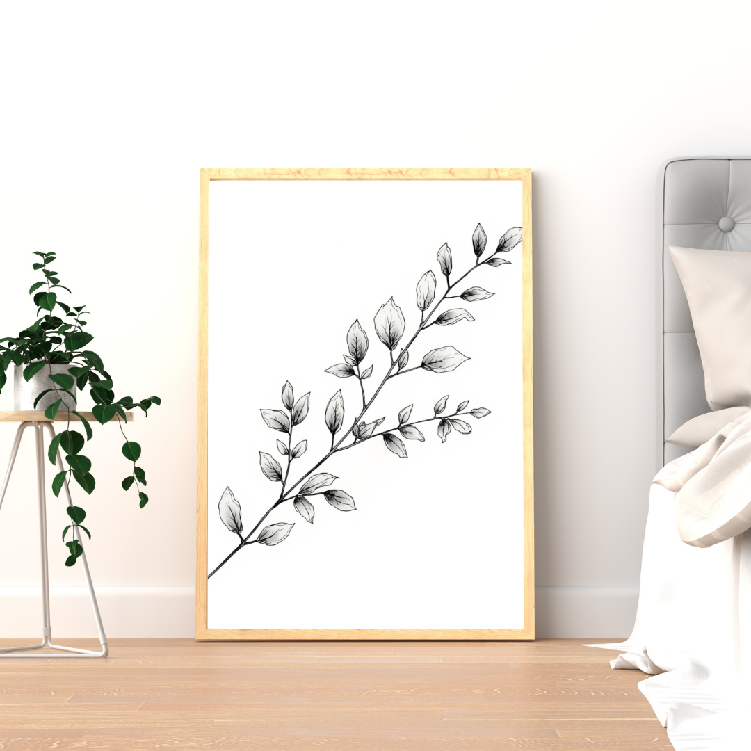 Botanische bladtak schilderij met fijne grijze bladtak en ovale blaadjes in gouden lijst staand op houten vloer naast groene plant – minimalistisch wall art logeerkamer
