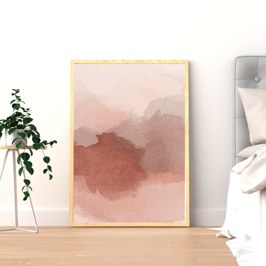 Abstract oudroze wolk schilderij met zachte oudroze en mauve wolkvlekken in gouden lijst staand op houten vloer naast groene plant – romantisch wall art logeerkamer
