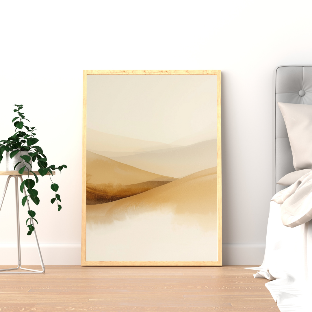 Abstract zandgolven schilderij met vloeiende beige en bruine duingolven in gouden lijst staand op houten vloer naast groene plant – sereen wall art logeerkamer
