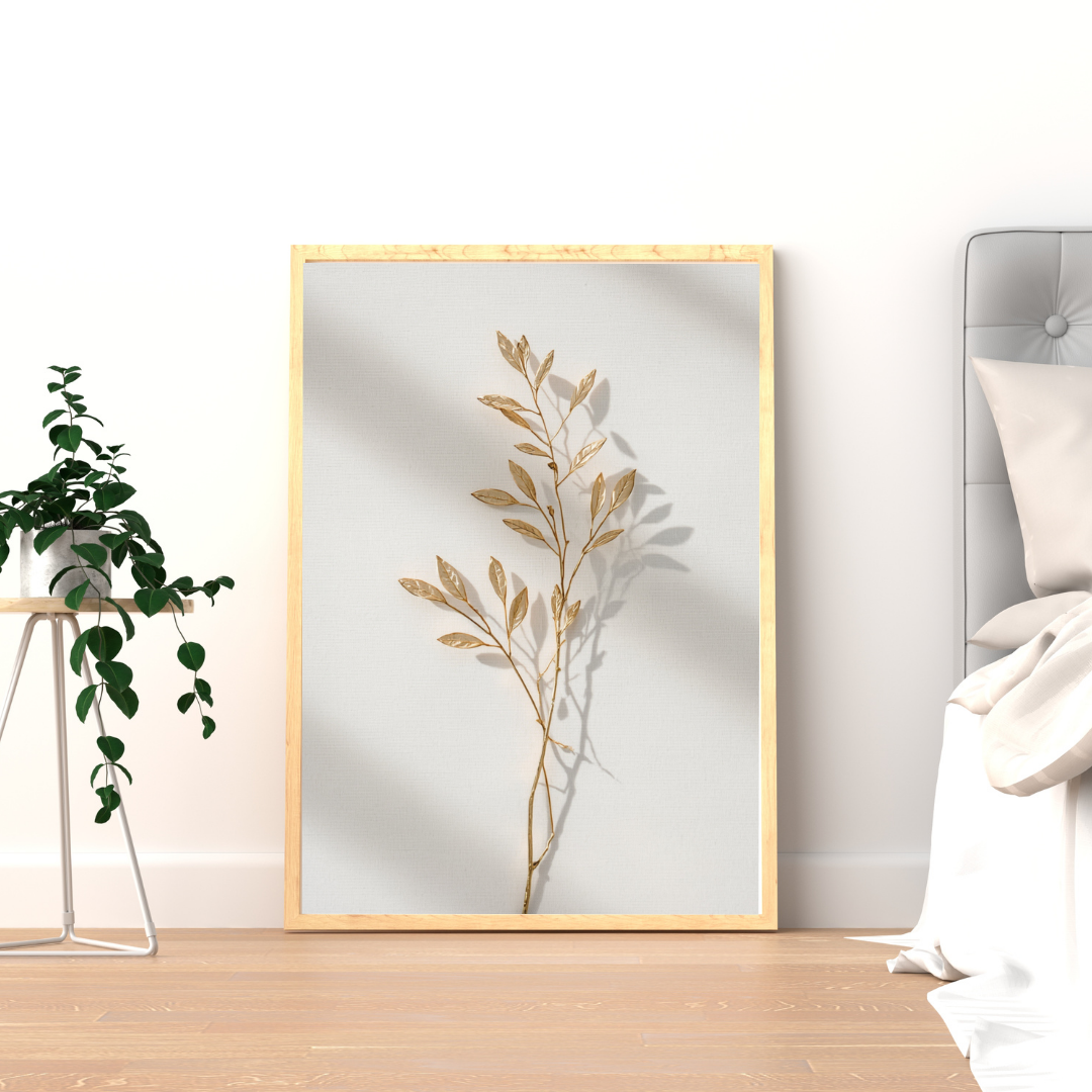 Botanische olijftak schilderij met droge beige olijftakken en schaduwspel in gouden lijst staand op houten vloer naast groene plant – naturel wall art logeerkamer

