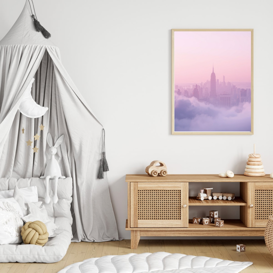 Mistige stadsskyline canvas schilderij in lichte lijst aan witte muur boven houten commode met hemelbed in zachte babykamer — roze lila wanddecoratie
