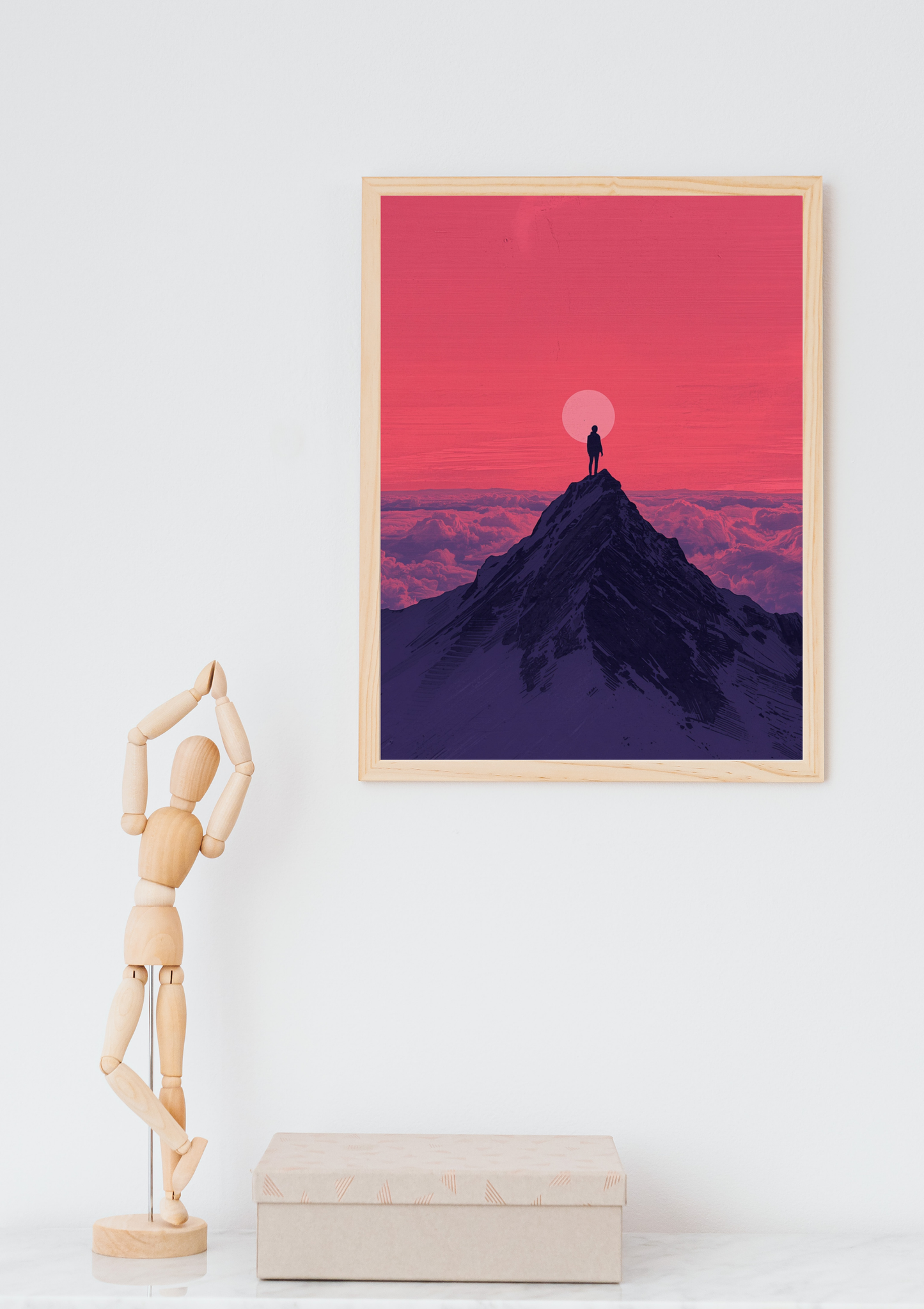 Bergpiek silhouet roze zonsondergang schilderij in naturel houten lijst aan witte muur naast houten paspop en beige doos – digitaal wall art thuiskantoor
