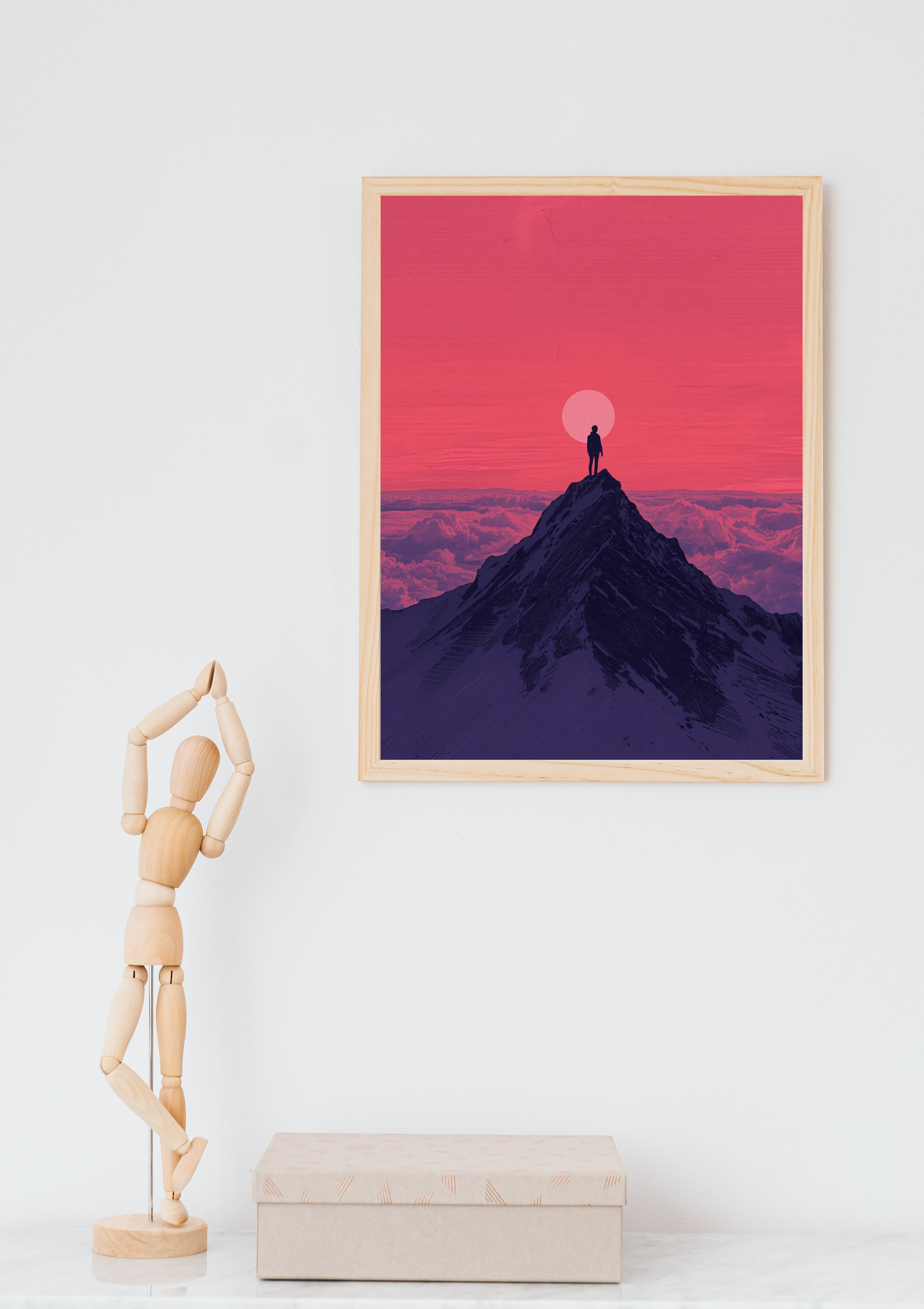 Bergpiek silhouet roze zonsondergang schilderij in naturel houten lijst aan witte muur naast houten paspop en beige doos – digitaal wall art thuiskantoor
